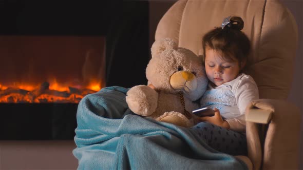 Little Girl Sitting on the Chair with Smartphone Hugging Toy Teddy Bear