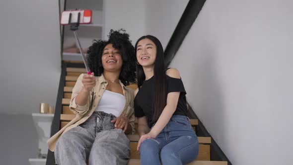 Portrait of Two Positive Women Taking Selfie on Smartphone Sitting on Stairs Talking and Smiling