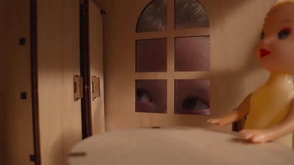 Interested Girl Peeks Into Window of Dollhouse in Dark Room
