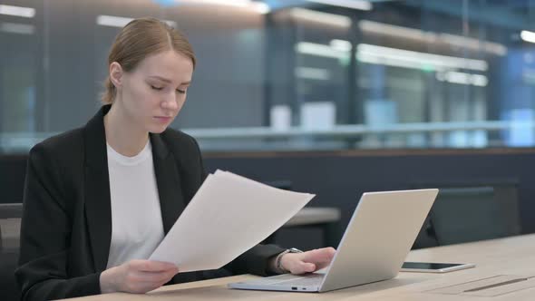 Businesswoman Reading Documents While Using Laptop