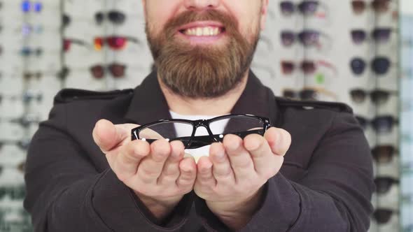 Bearded Man Smiling Holding Out Glasses To the Camera