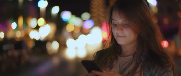 A young woman listening to the music on her phone in the middle of a street