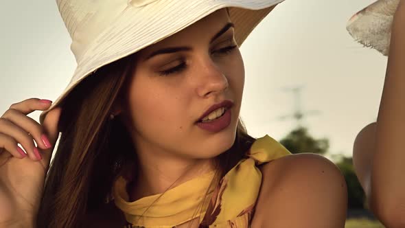 Model in a Hat Sits in the Field and Adjusts His Hair. Slow Motion. Close Up