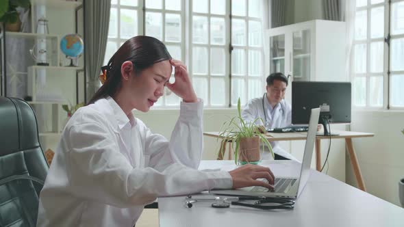 Young Asian Woman Doctor Is Using Laptop Computer And Headache In Workplace. Medical Concept