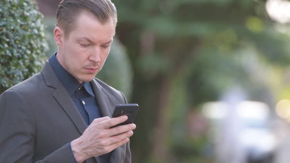 Face of Happy Young Handsome Businessman Using Phone Outdoors