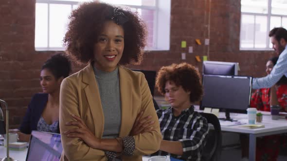 Mixed race businesswoman sitting smiling in office room with diverse colleagues in background
