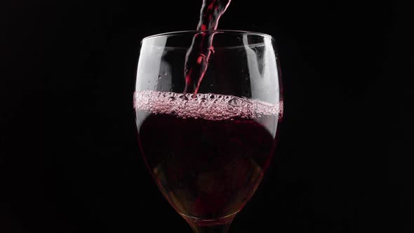 Wine. Red wine pouring in wine glass over dark background. Rose wine pouring from the bottle. Slow m