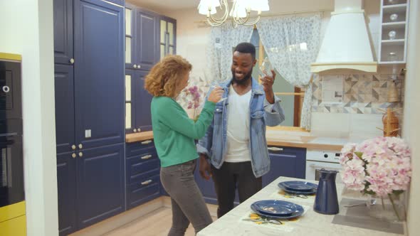 Happy Diverse Couple Clinking Empty Wine Glasses in Brand New Kitchen
