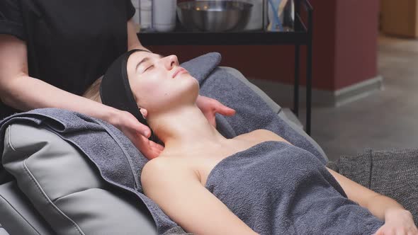 An Attractive Woman Lies on a Bed in a Beauty Salon and Gets a Massage on the Decollete and Neck