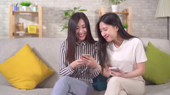 Two Happy Young Asian Girls with Smartphones on the Sofa in the Living Room