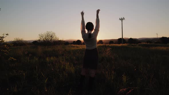 girl raises her hands in a field at sunset