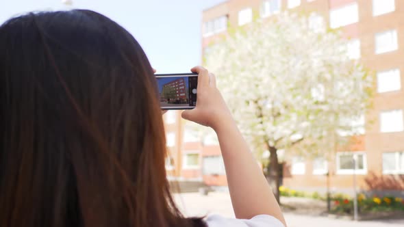 Back view of Asian Straight hair woman standing at a street and taking a photo of buildings view