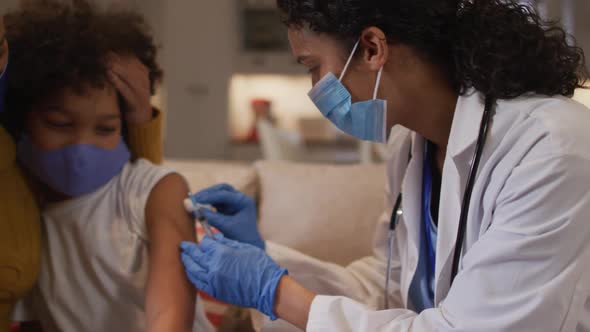 Mixed race female doctor wearing face mask making injection at home