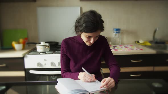 Cute Lefthanded Girl Learning to Write with Her Right Hand Sitting at the Table