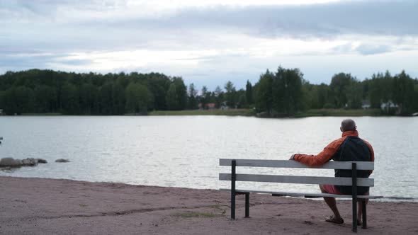 Senior Man Sitting On The Bench By The Lake