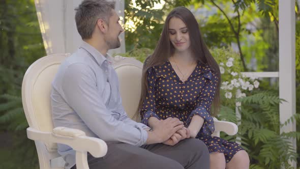 Loving Caucasian Couple Sitting Outdoors Holding Hands. Portrait of Relaxed Happy Man and Woman