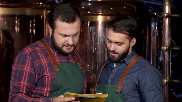 Two Beer Makers Smiling To the Camera, While Working at Their Brewery