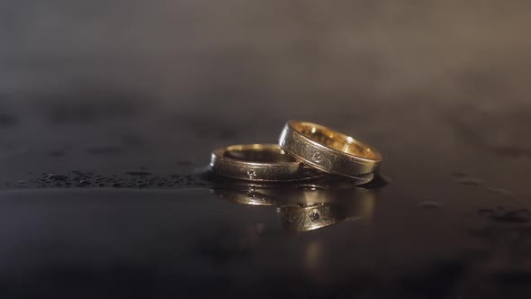 Wedding Rings on Dark Water Surface Shining with Light. Close Up Macro