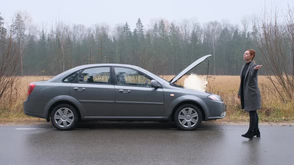 A Woman Stands By the Road Near a Broken Car