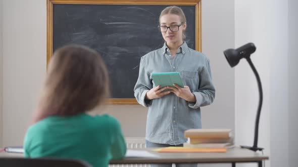 Portrait of Positive Caucasian Female Teacher in Eyeglasses Talking with Pupil Indoors in School