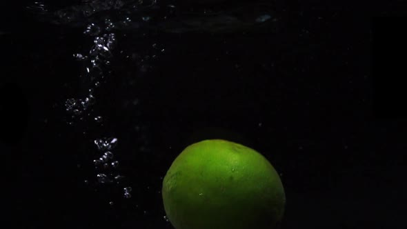 Green Lime Are Thrown Into a Container of Water. Video of Fruit in Slow Motion. Food Video.