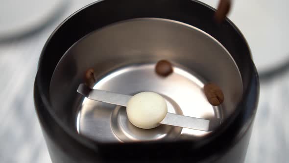 Roasted coffee beans fill the electric grinder as they fall onto the stainless, shiny blades