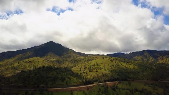 Aerial pan, highway winding along lush green mountains in California, cloudy day