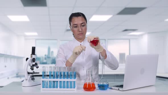 A Female Scientist Pours Red Liquid From a Flask Into a Test Tube and Does Clinical Trials