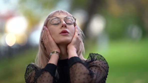 Close-up Portrait of a Young Positive Blonde Woman with Glasses Posing Straightening Her Hair While