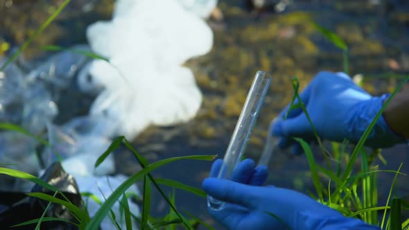 Scientist With Tube Taking Water Sample From Polluted Lake, Plastic Waste