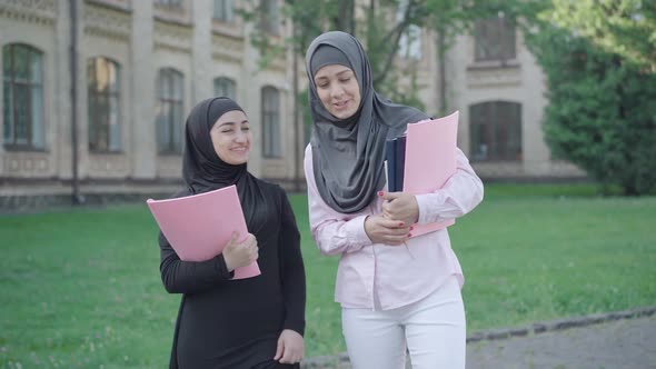 Portrait of Two Confident Muslim Women Walking on University Yard and Talking. Young Female