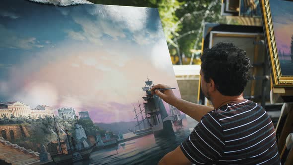 Male Artist Drawing a Picture with Marine Landscape Sailing Ships and City on Coast While Sitting in