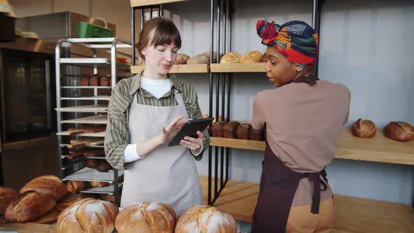 Two Multiethnic Women Using Tablet and Working in Bakery