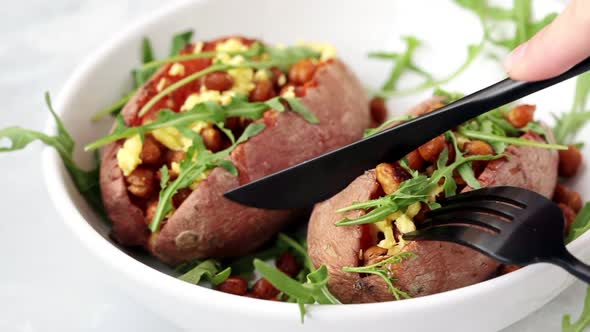 Eating Baked Sweet Potato Stuffed with Fried Chickpeas and Vegan Cheese on White Background. Healthy