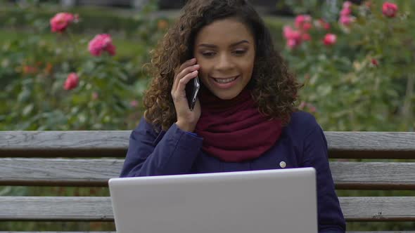 Biracial Female Journalist Sitting at Park and Calling Employer, Freelancer