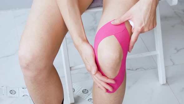 Young Woman Makes Herself Taping a Knee Post-rehab-sitting