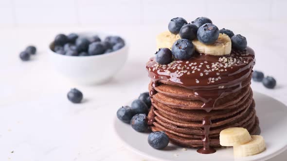 Stack of chocolate pancakes with chocolate sauce, blueberries and banana.