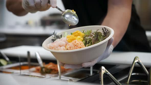 Worker scoops and adds chopped mango to poke bowl salad, slow motion 4K