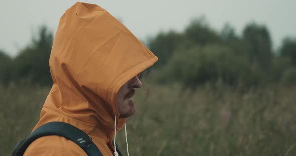 Man with Beard Dressed in an Raincoat with Hood Admires View of Nature at Sunset