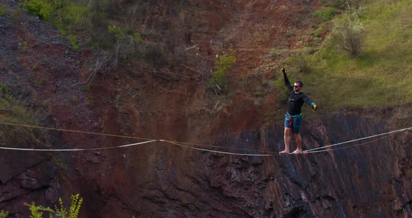 Slackliner Is Walking on the Tightrope Over a Quarry Sitting Down