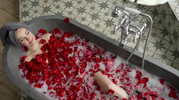 Sexy Girl Lies in a Big Stone Bath with a Rose Flower in Her Hands