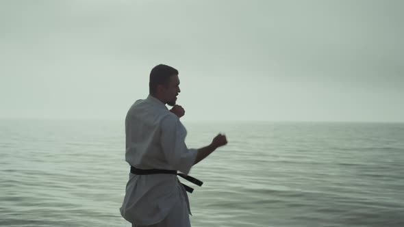 Strong Man Practicing Taekwondo Near Ocean Against Cloudy Sky in Slow Motion