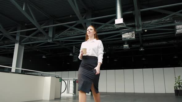 female leader walks through lobby of business center with a phone and cup coffee