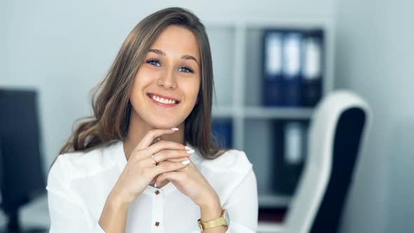 Cheerful Businesswoman Sitting at the Table in Office and Looking at Camera