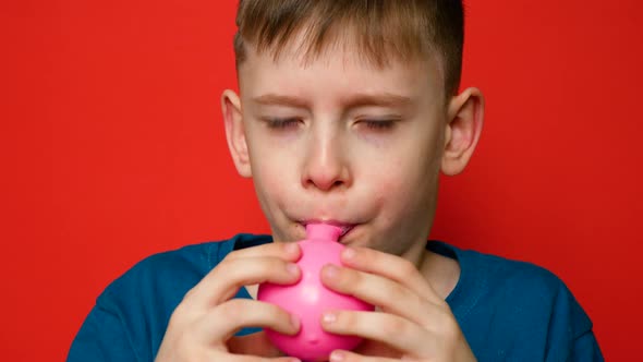 Portrait Caucasian boy 7-8 years old inflates a balloon with his mouth and looks at the camera on a