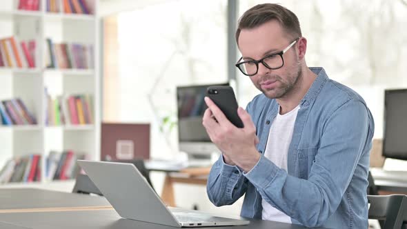 Young Man Using Smartphone and Laptop