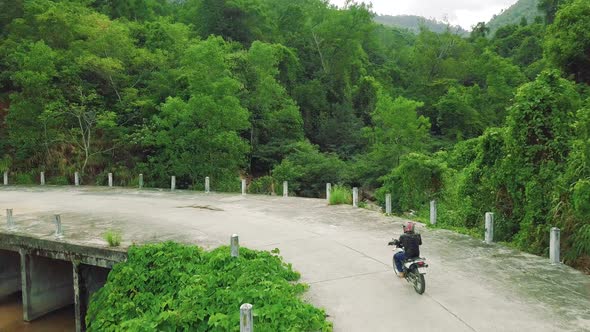 Aerial View of a Motorcycle Rider Driving Bike Along a Bridge in Countryside.