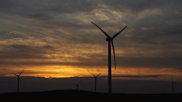 Motion the Blades of a Large Wind Turbine in a Field Against a Background of Orange Sunset on the