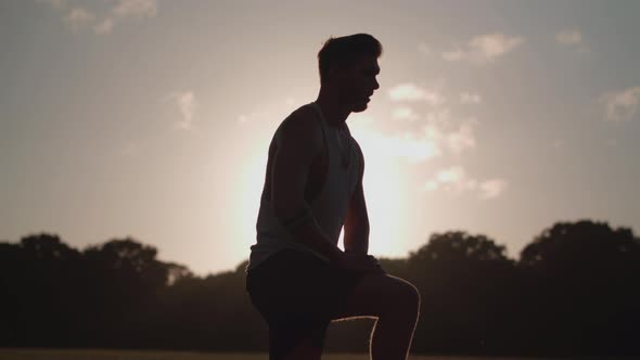 Man Stretching His Legs Before a Run Whilst Being Silhouetted By The Evening Sun