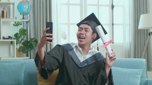 Excited Asian Man Showing Off A University Certificate During An Online Video Call By Mobile Phone